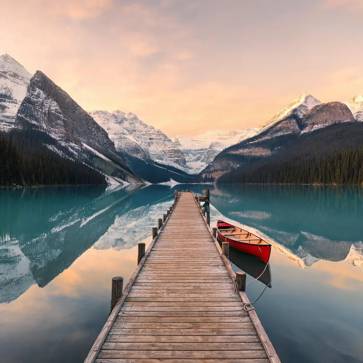 A wooden dock and red canoe on a mountain lake