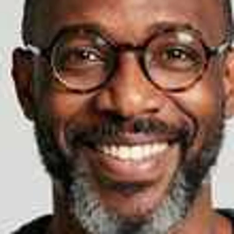 Close-up of a smiling man with round glasses and a gray beard from a 240 pixel image, soft and grainy
